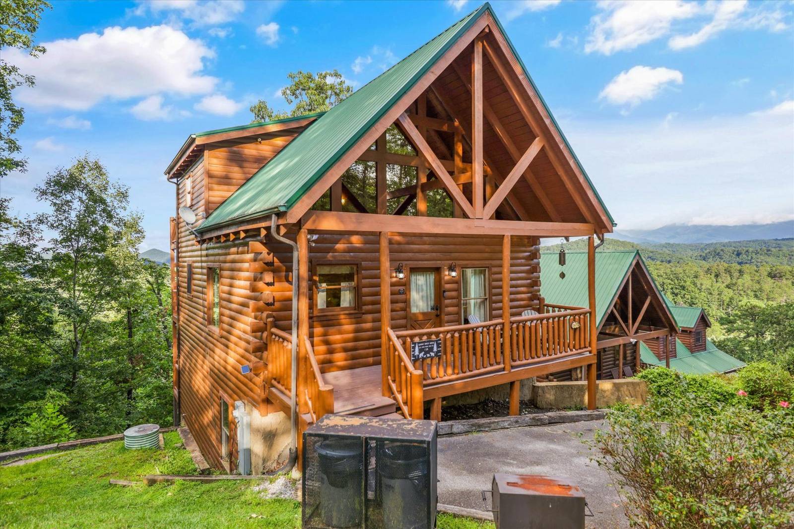 Wooden log cabin with green roof and front porch among green trees