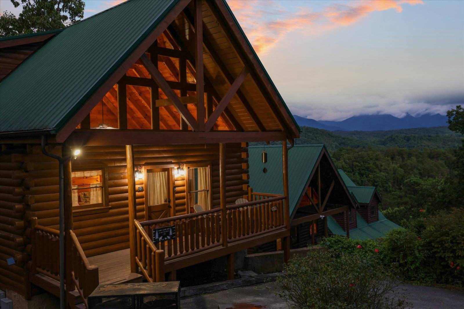 Log cabin with lighted windows and deck, mountains in background