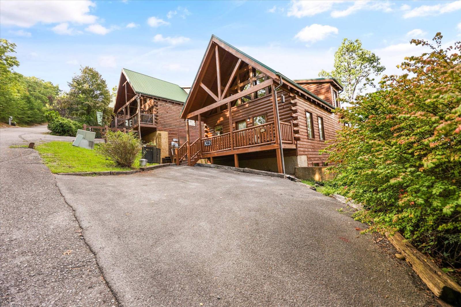 Two wooden log cabins with green roofs and a driveway
