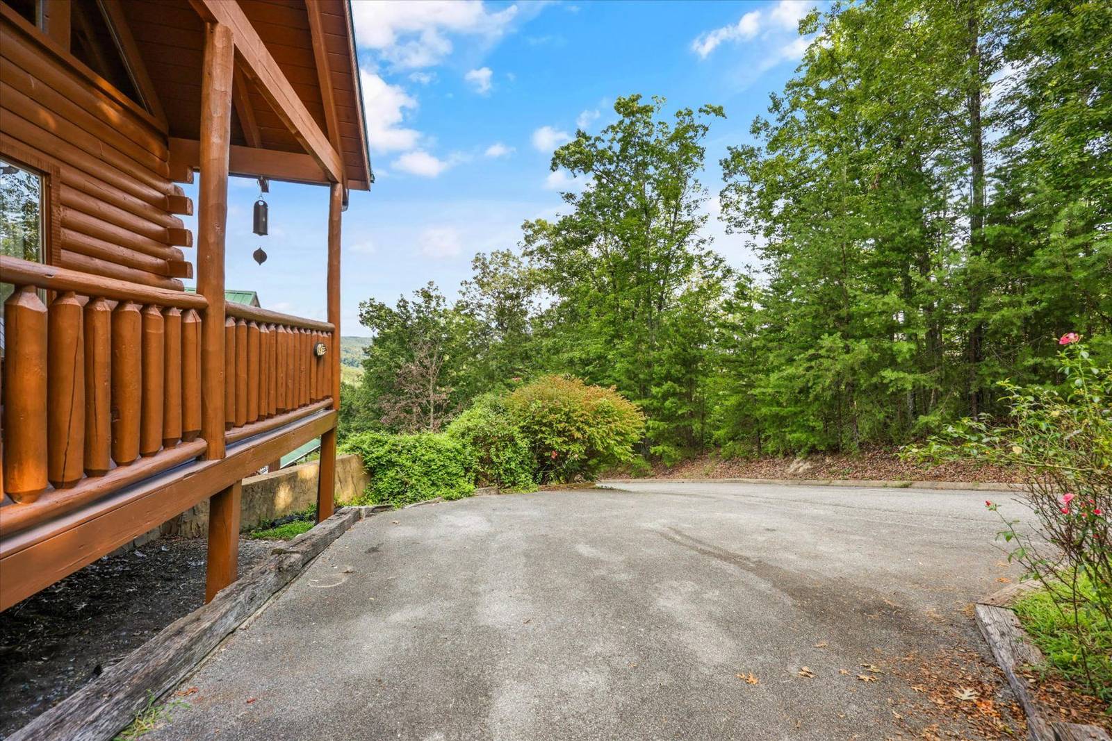 Wooden cabin balcony next to a paved driveway surrounded by trees