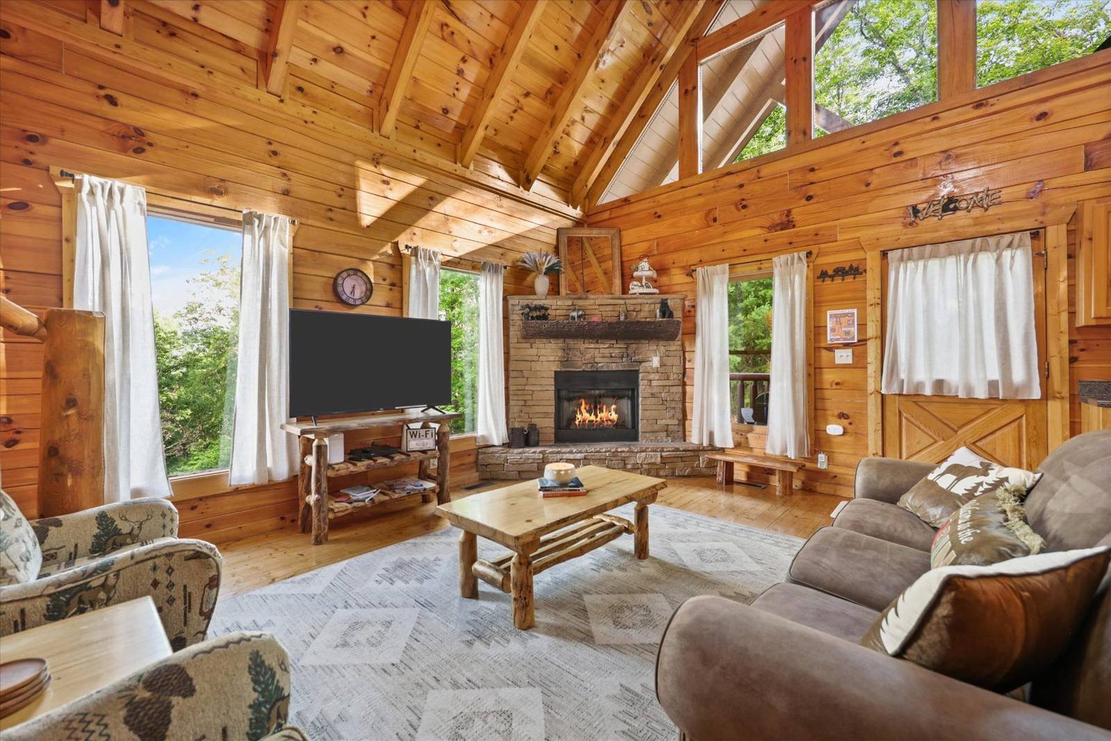 Wood paneled living room with stone fireplace, television, sofa, and armchairs