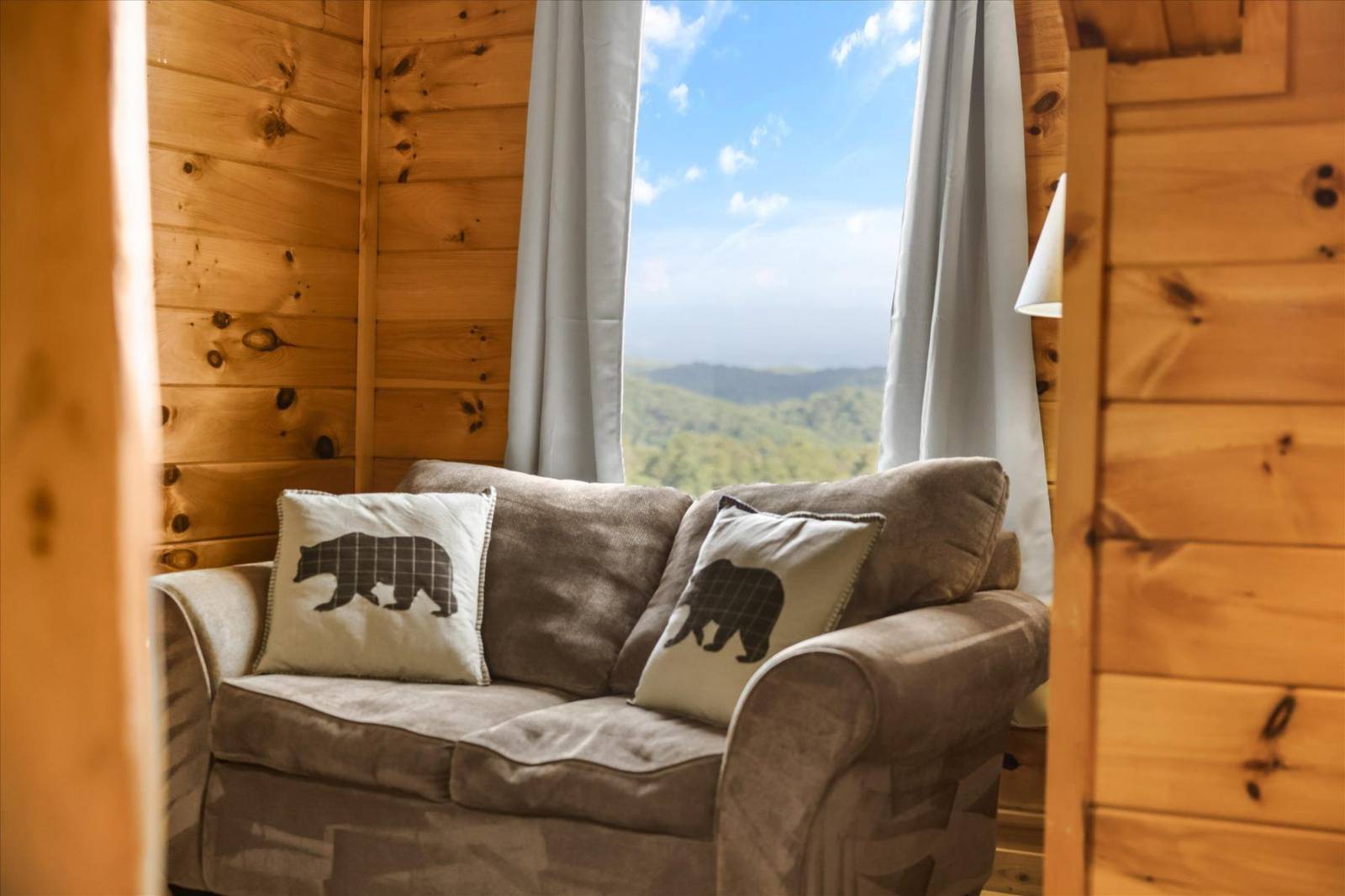 Brown couch with bear pillows by a window revealing green mountains and sky