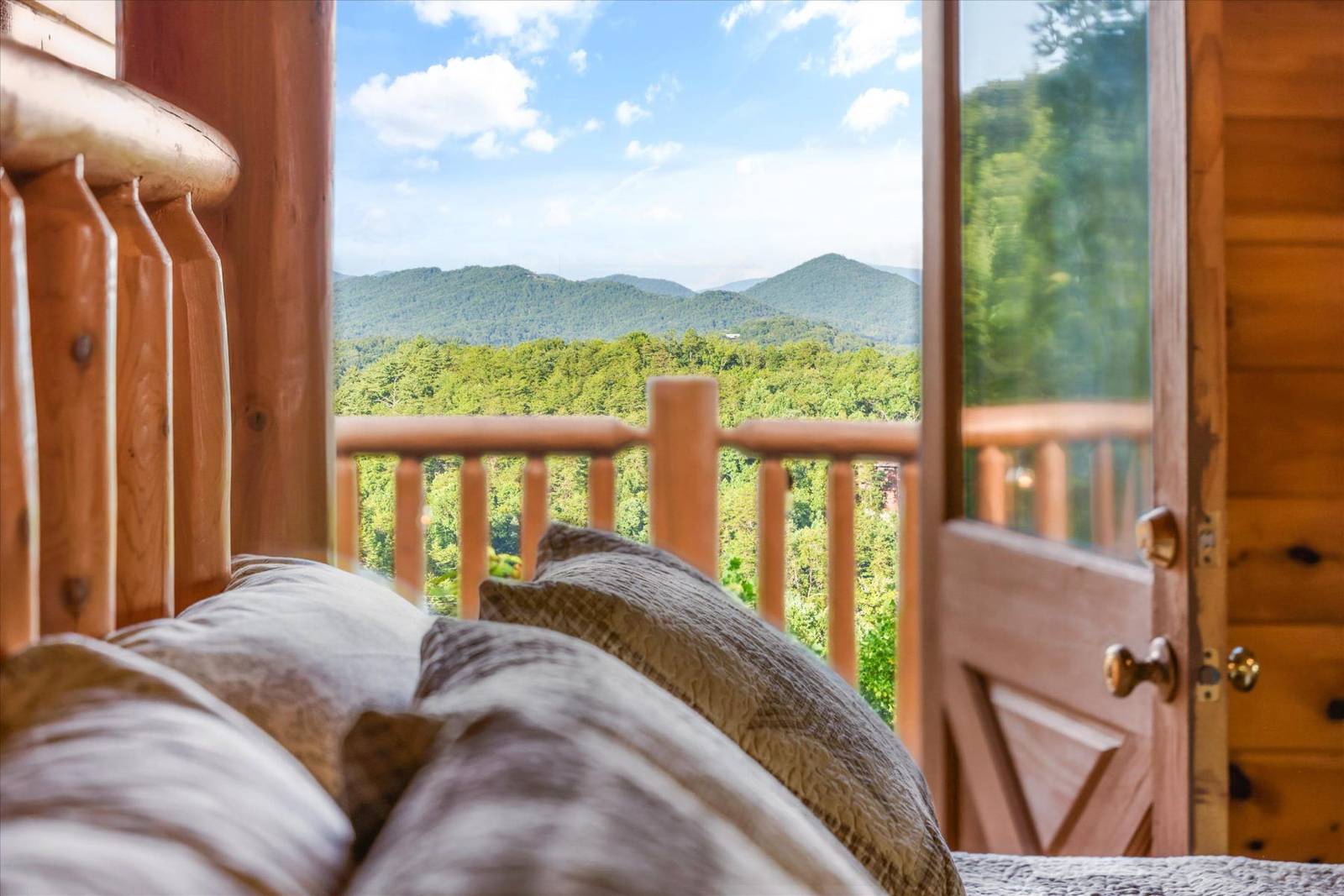 Bed with pillows facing mountain view through open door and railing