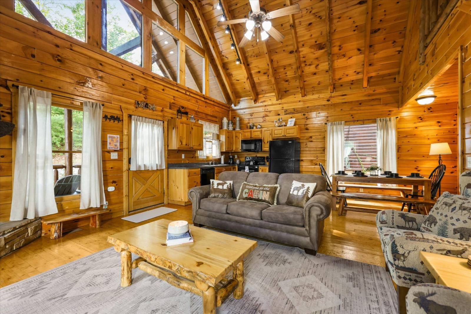 Rustic cabin great room with wood paneling, sofa, and kitchen