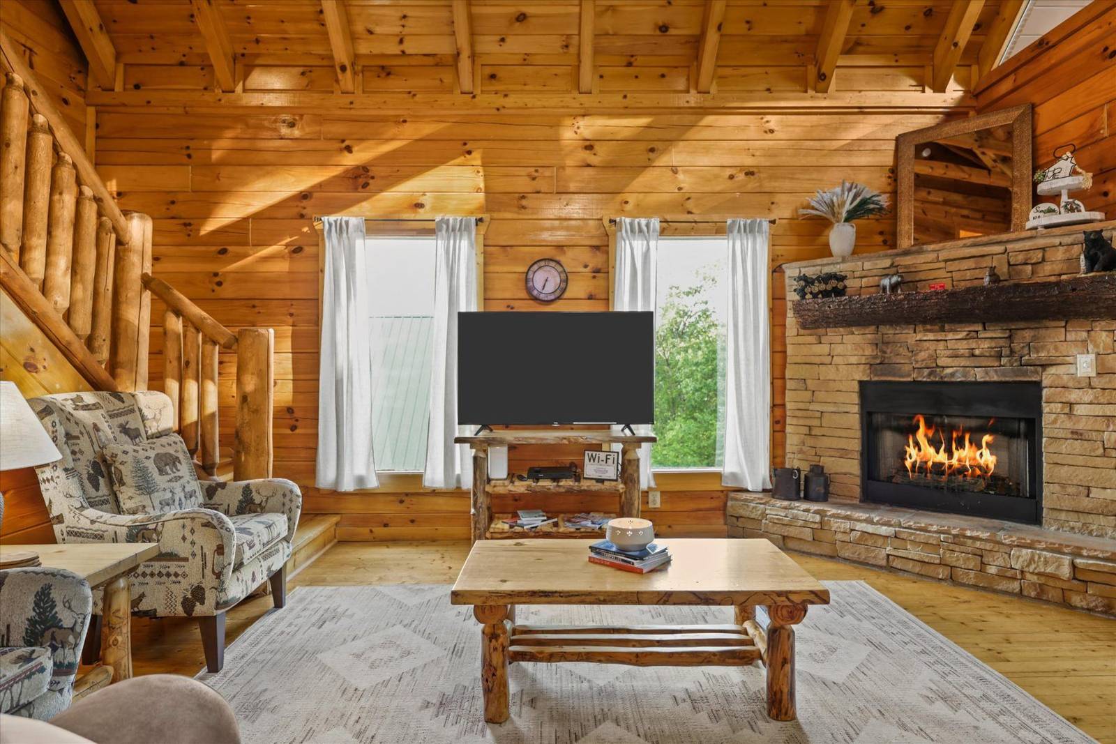 Cozy great room with stone fireplace, television, wooden furniture, and stairs
