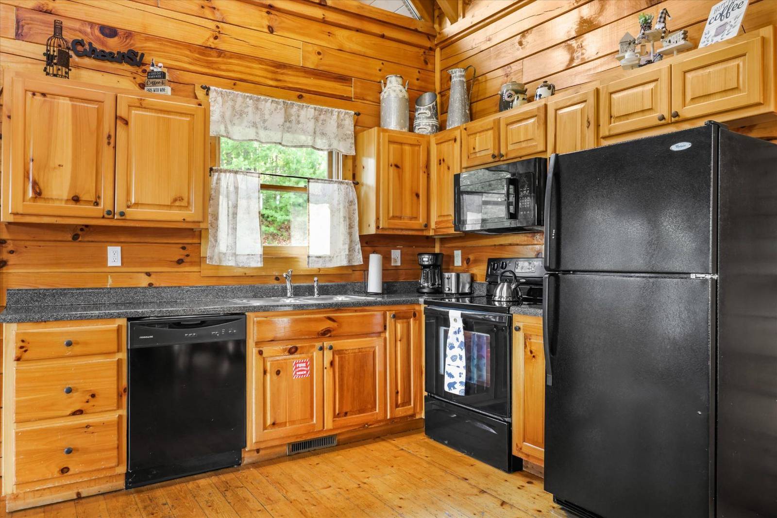 Rustic kitchen with wooden cabinets, black appliances, and a window
