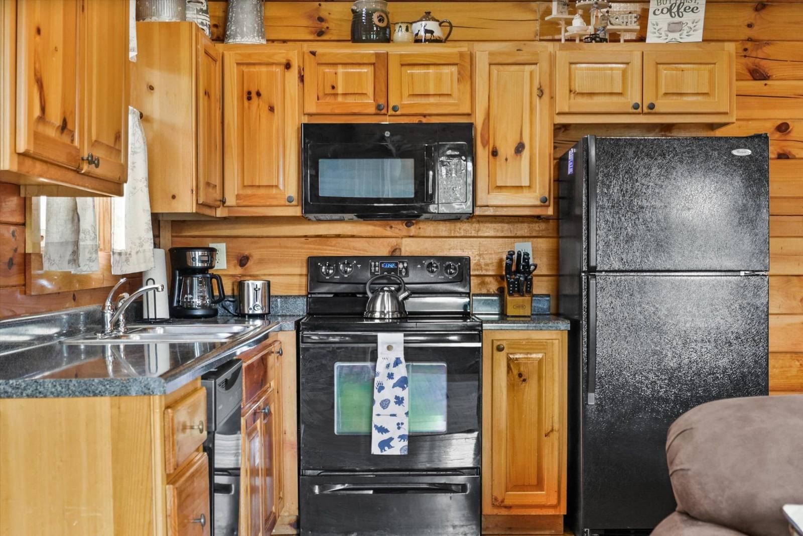 Kitchen with wooden cabinets, black appliances, sink, and log walls