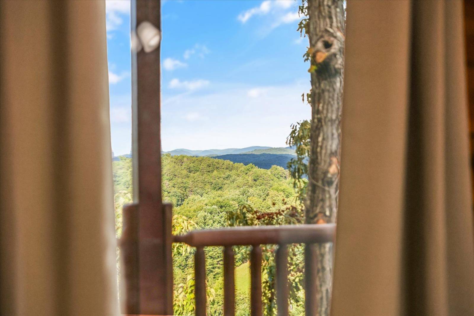 Window view of green forested mountains, blue sky, and a wooden railing