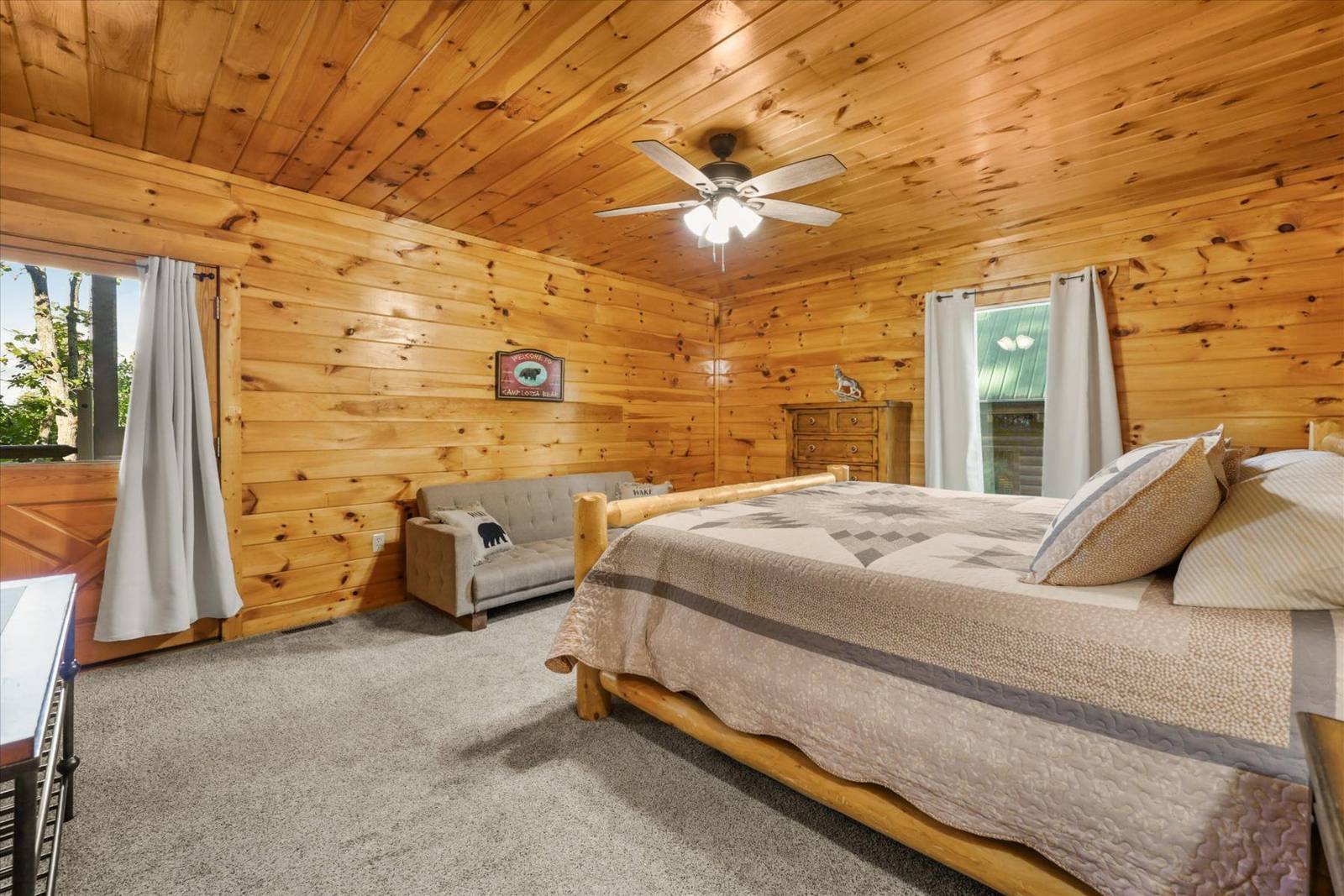 Wood-paneled bedroom with a large bed, sofa, dresser, and ceiling fan