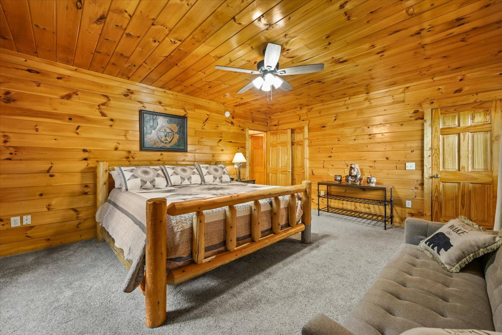 Wood-paneled bedroom with rustic bed frame, grey carpet, and ceiling fan