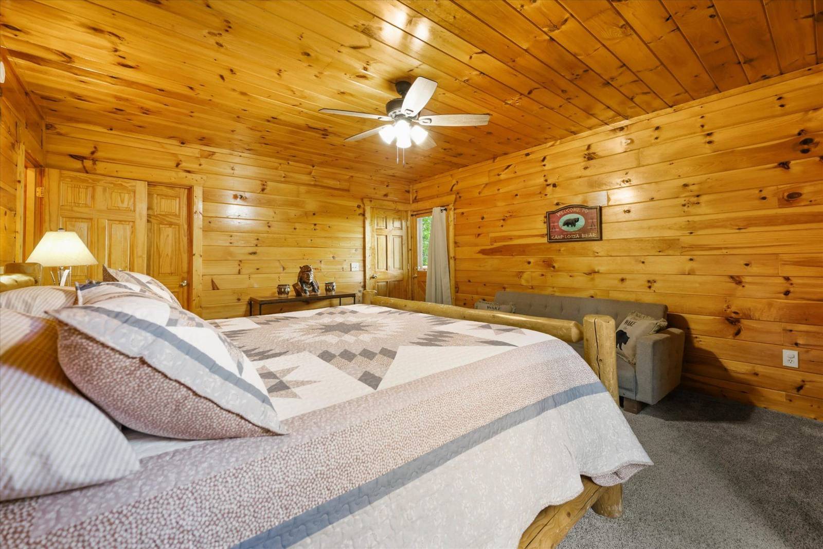 Bedroom with wooden walls, patterned quilt, small sofa, and ceiling fan