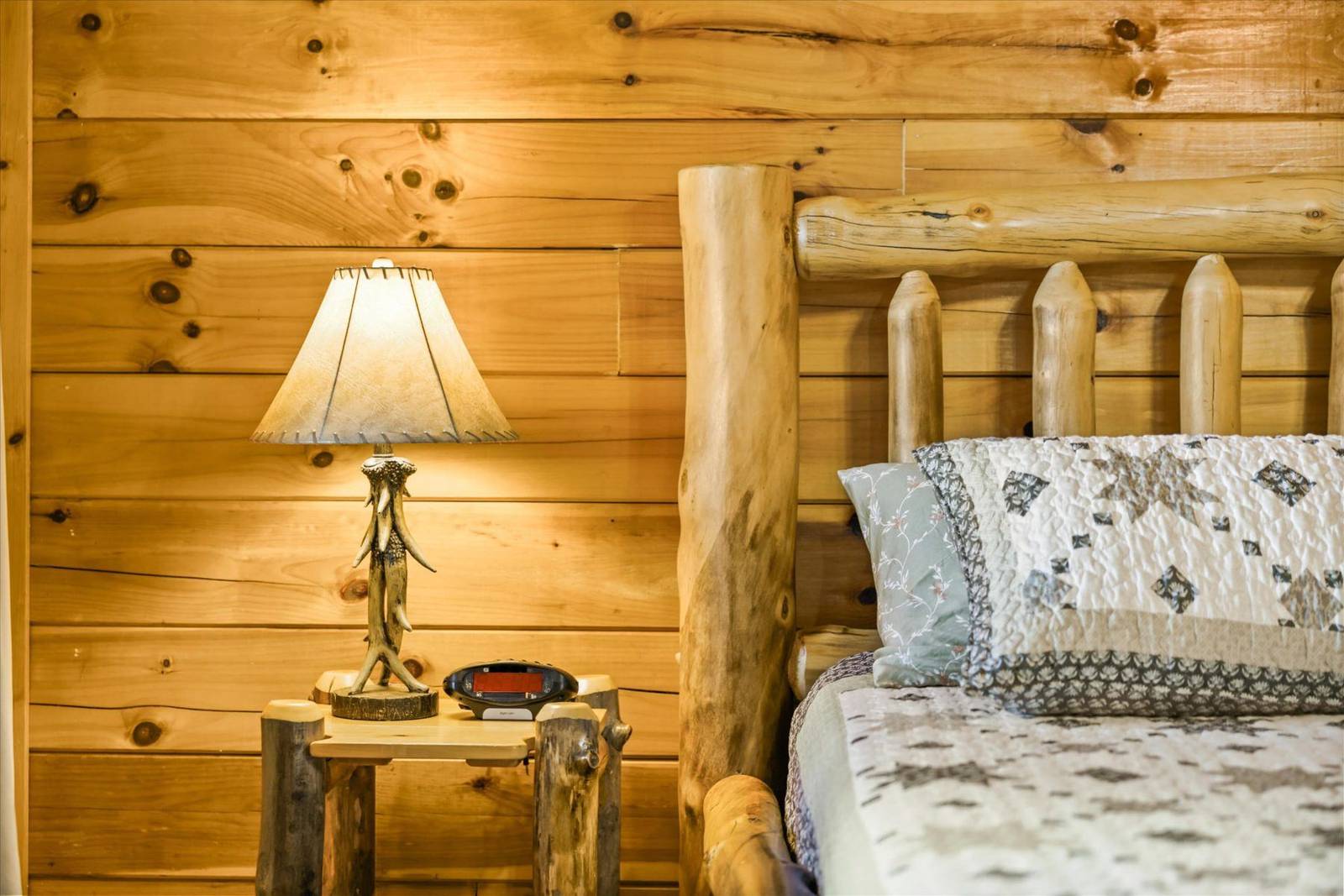 Log bed frame with quilted bedding, a rustic lamp, and wooden walls