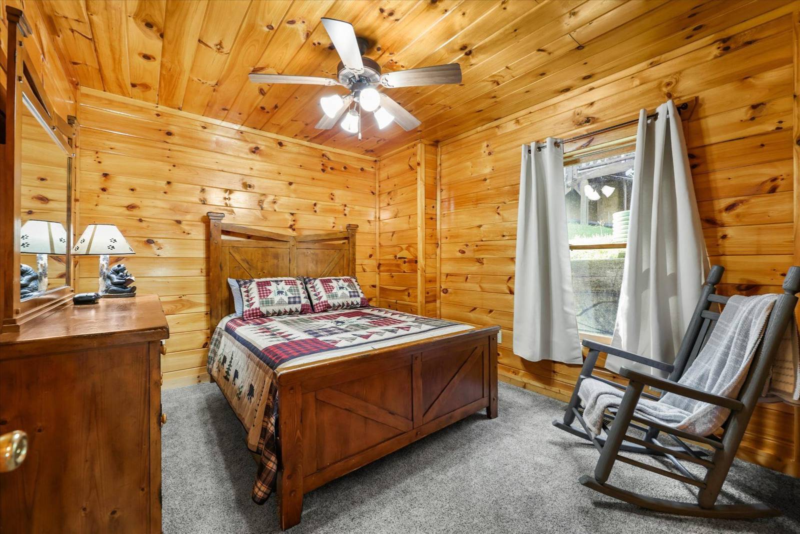Bedroom with wooden walls, bed, dresser, window, and rocking chair