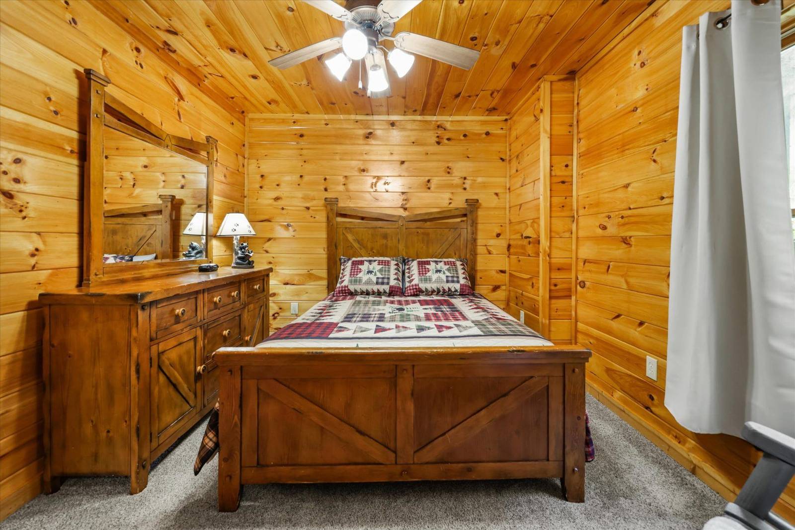 Bedroom with wooden bed, dresser, mirror, wood-paneled walls, and ceiling fan