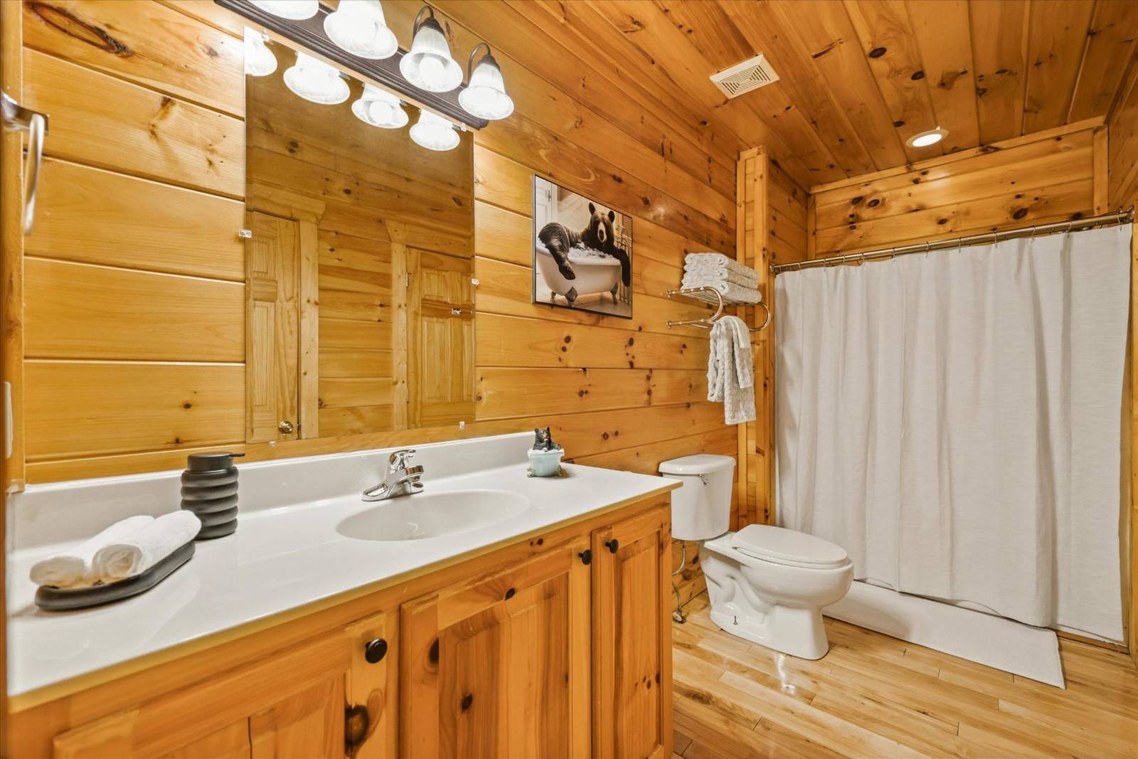 Wood-paneled bathroom with vanity, toilet, and shower with white curtain