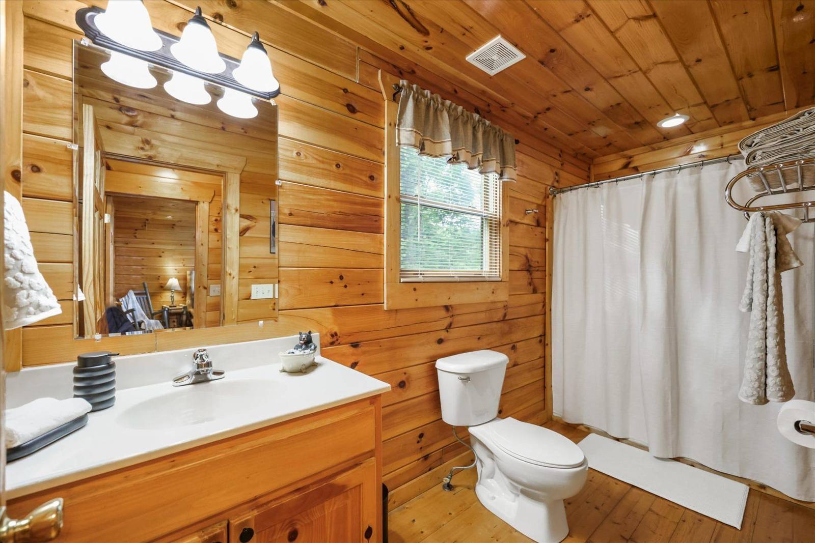 Rustic wood-paneled bathroom with vanity, toilet, and white shower curtain