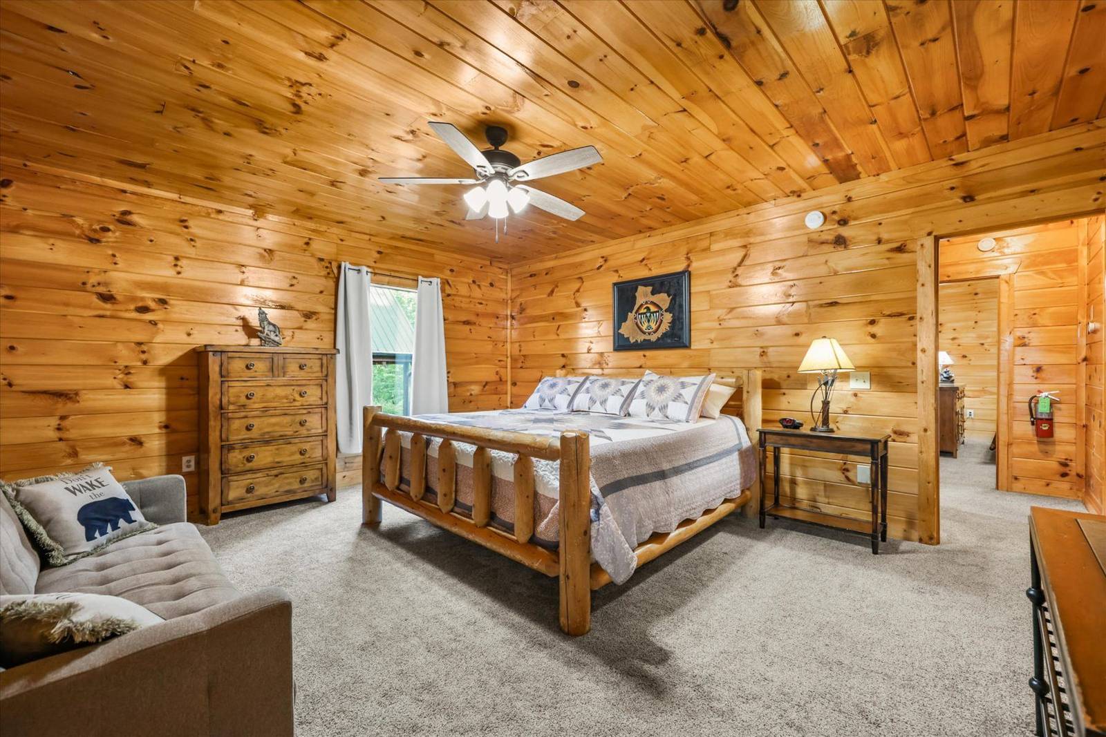 Wood-paneled bedroom with bed, dresser, sofa, and ceiling fan