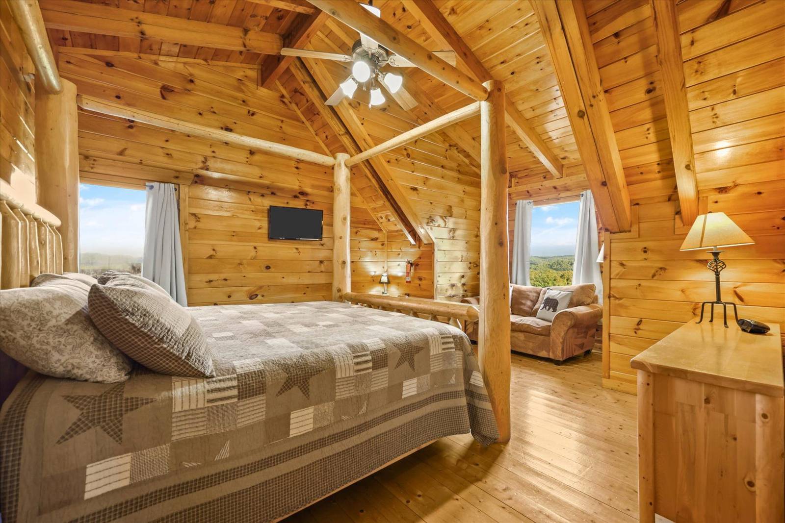 Log cabin bedroom with bed, TV, sofa, and window views