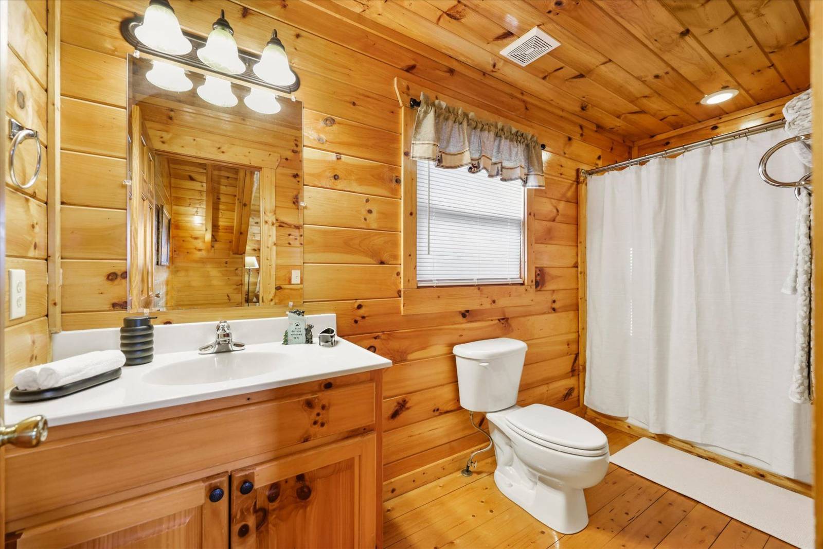 Wood-paneled bathroom with vanity, toilet, and white shower curtain