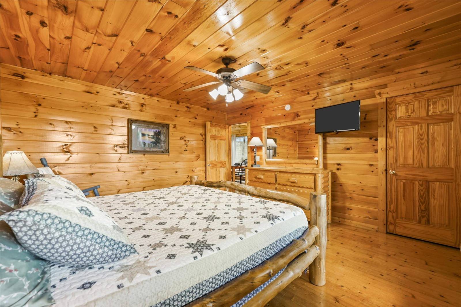 Wood-paneled bedroom with rustic bed frame, star quilt, dresser, and TV