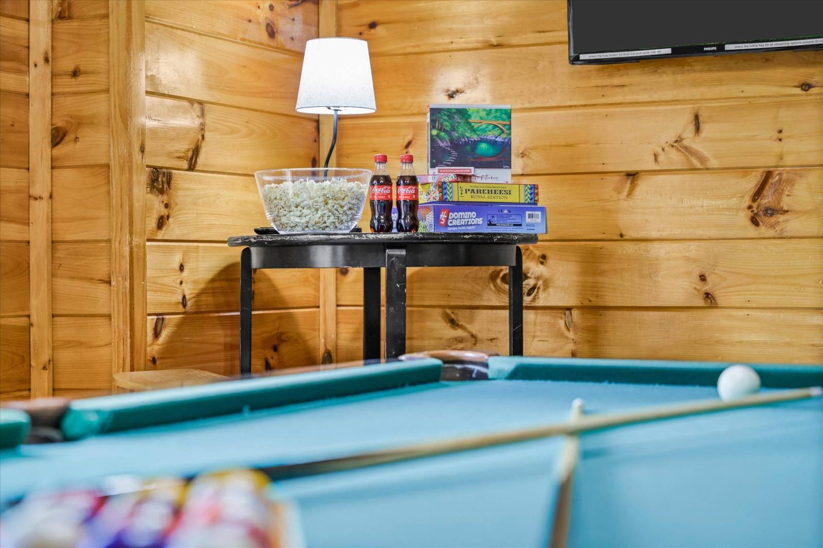 Pool table with games, snacks, and lamp against a wooden wall