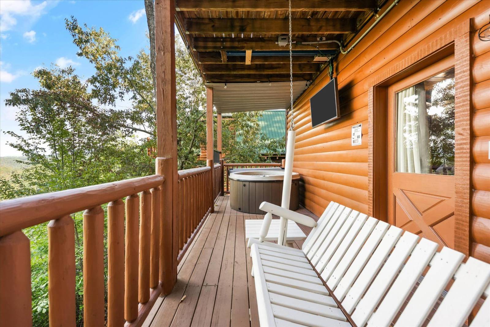 Wooden deck with hot tub, swing, outdoor TV, and forest view