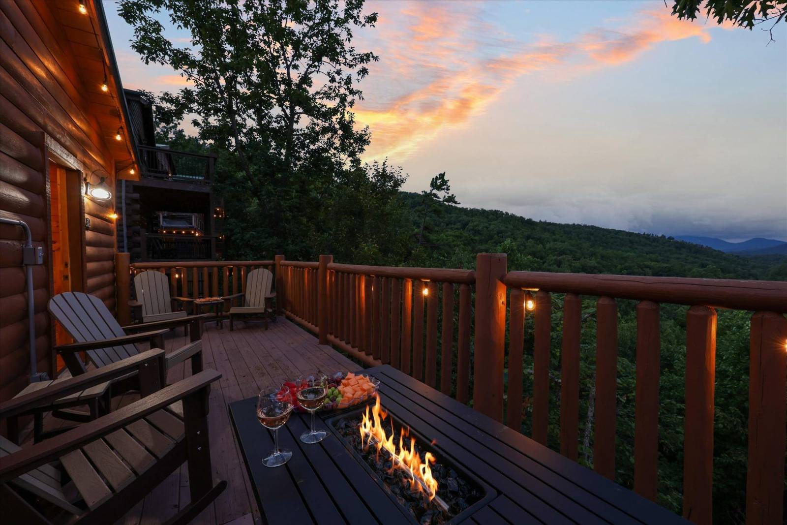 Deck with fire pit, wine, chairs, string lights, and sunset mountain view