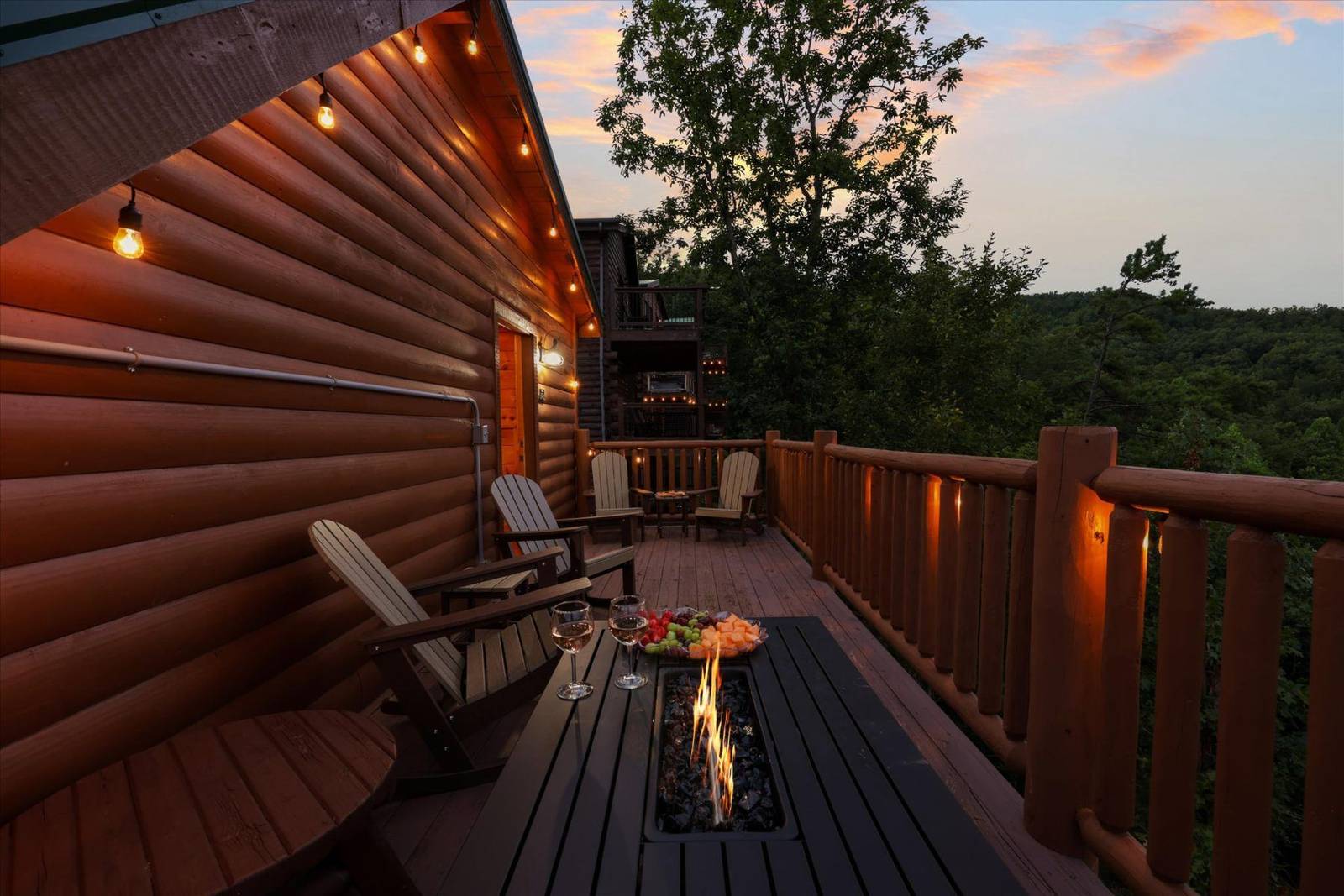 Wooden deck with fire pit, chairs, snacks, and string lights at dusk