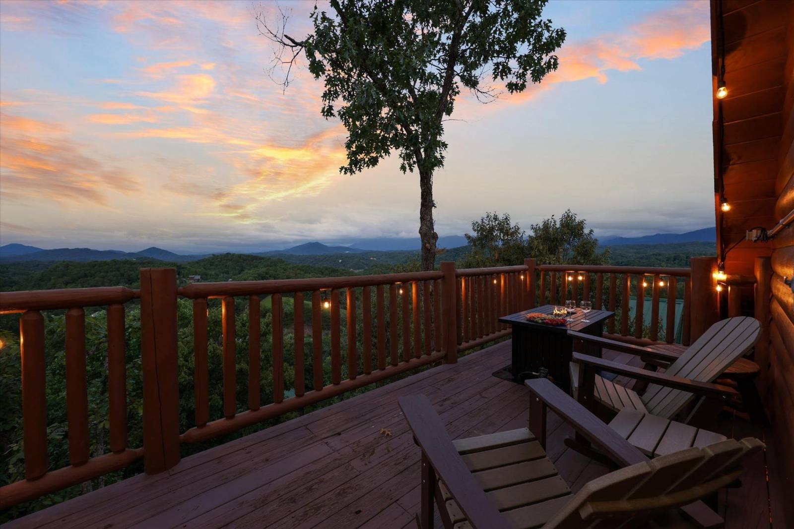 Wooden deck with Adirondack chairs and a table overlooking mountains at sunset