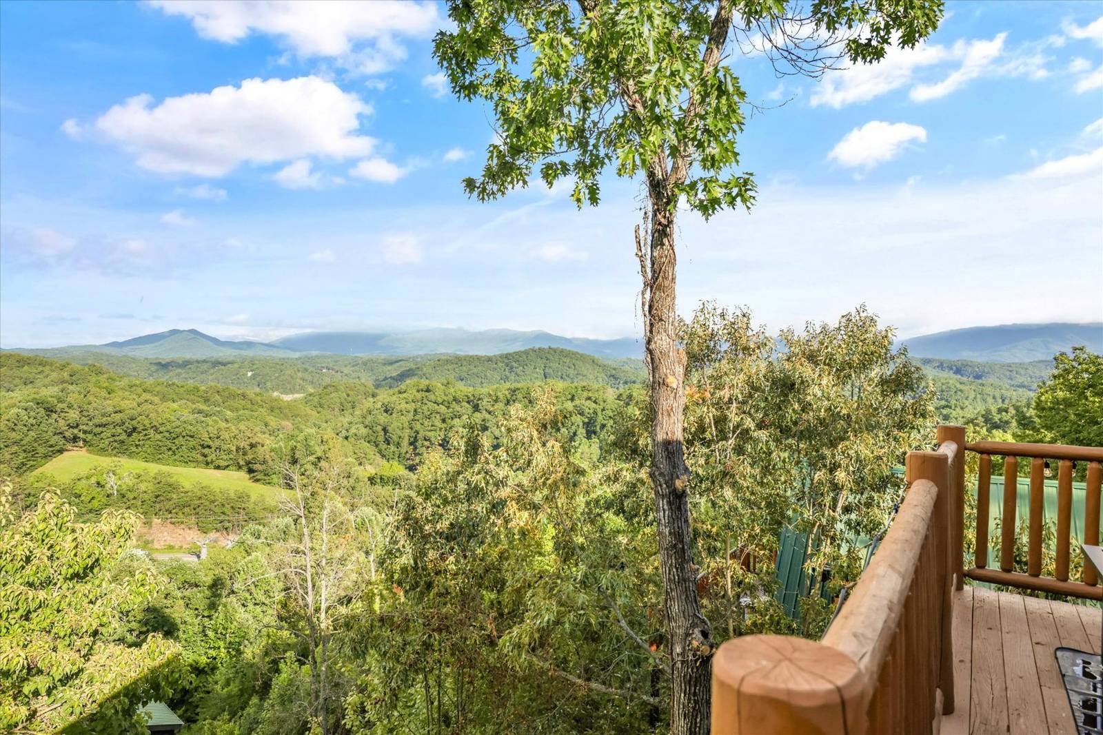 Expansive view of green mountains, hills, and sky from a wooden deck