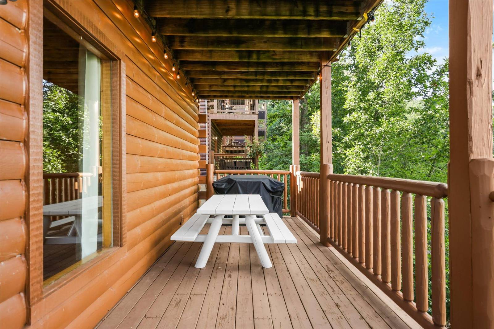 Wood deck with white picnic table and covered grill, surrounded by trees