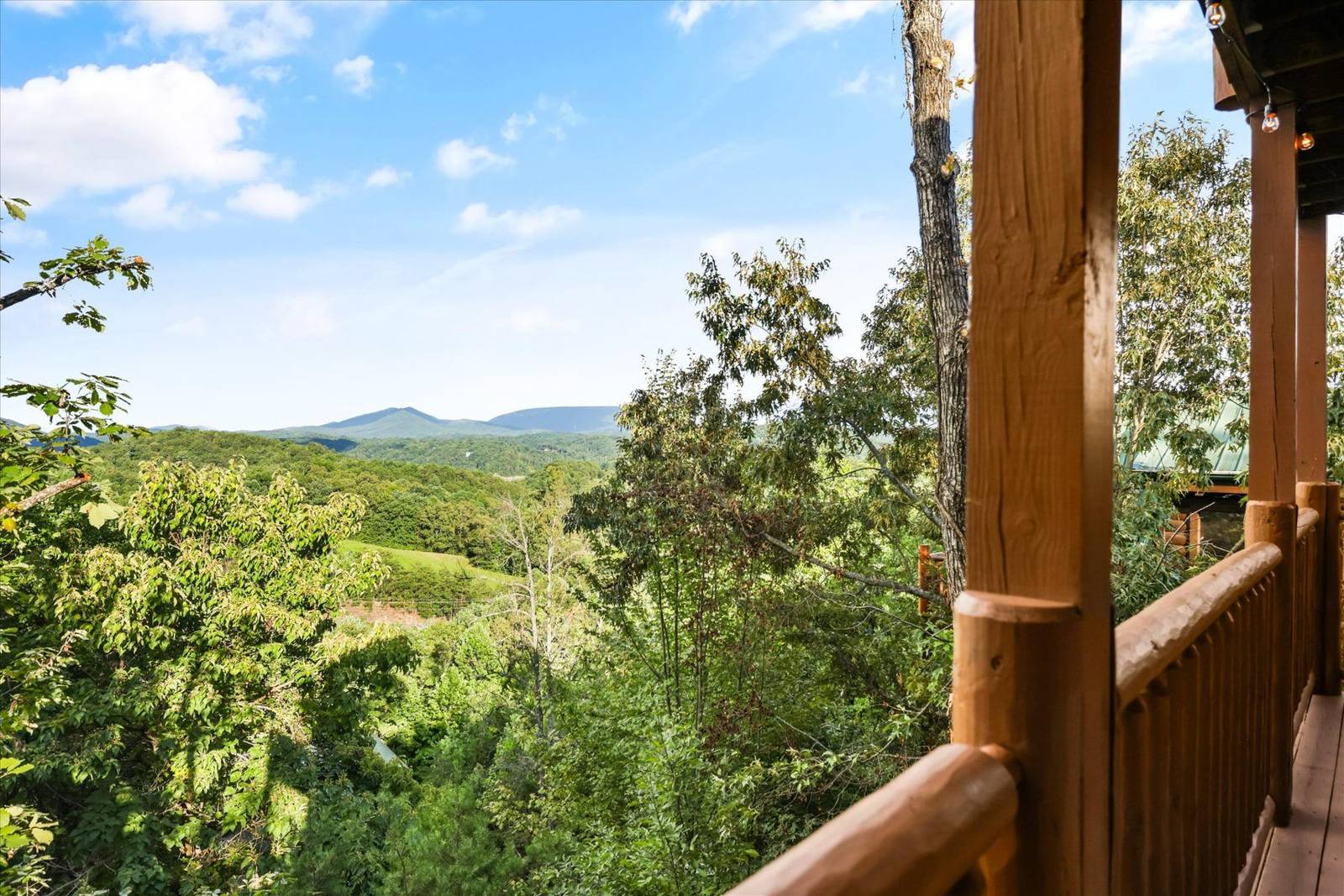 Wooden balcony overlooking forested hills and distant mountains under a blue sky