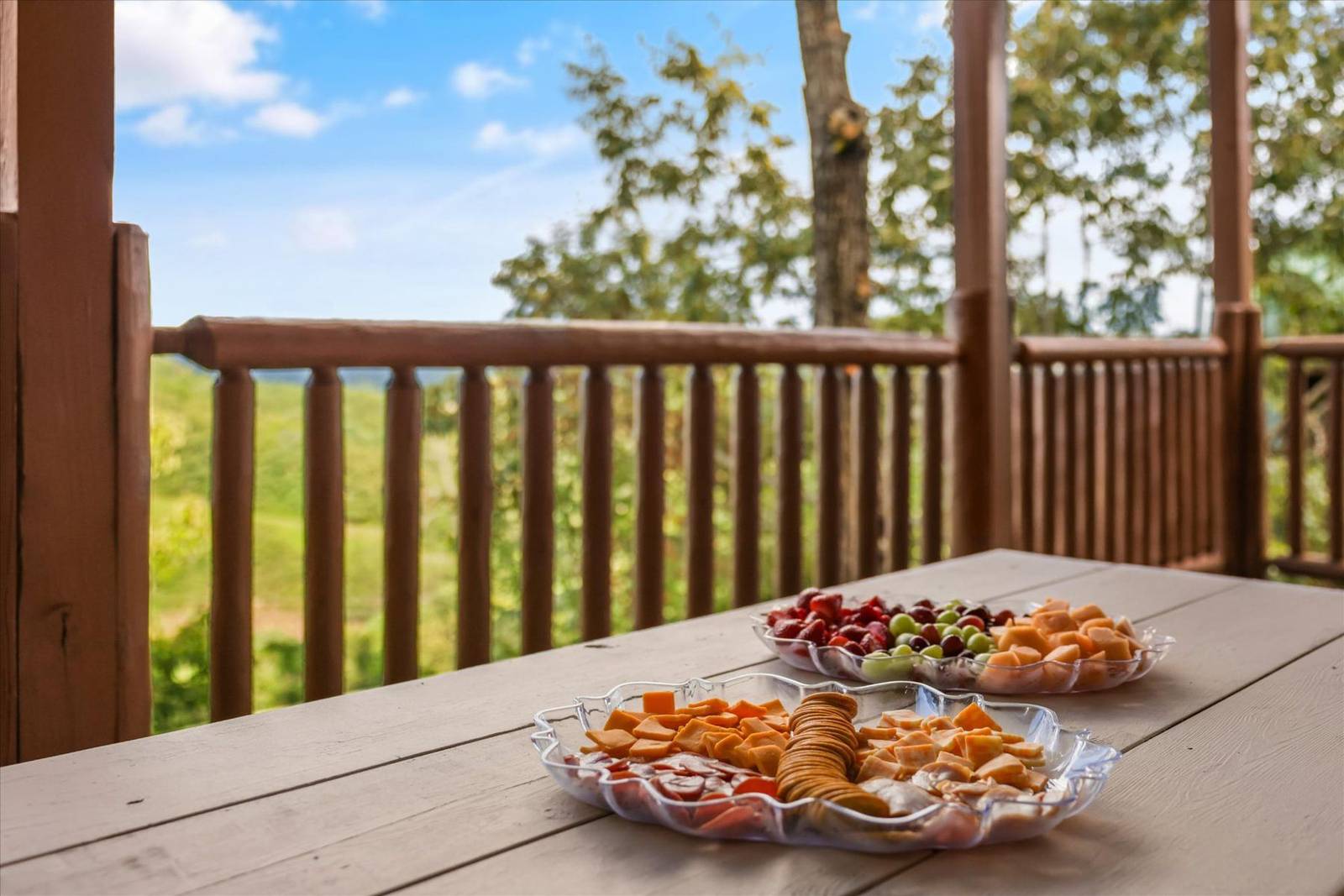 Two platters of snacks on a deck table with a wooded view