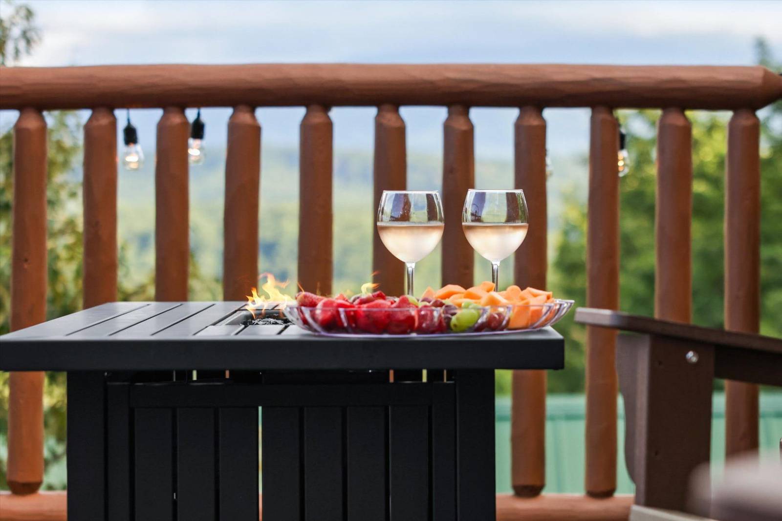 Fire pit table with wine glasses, fruit, and wooden railing