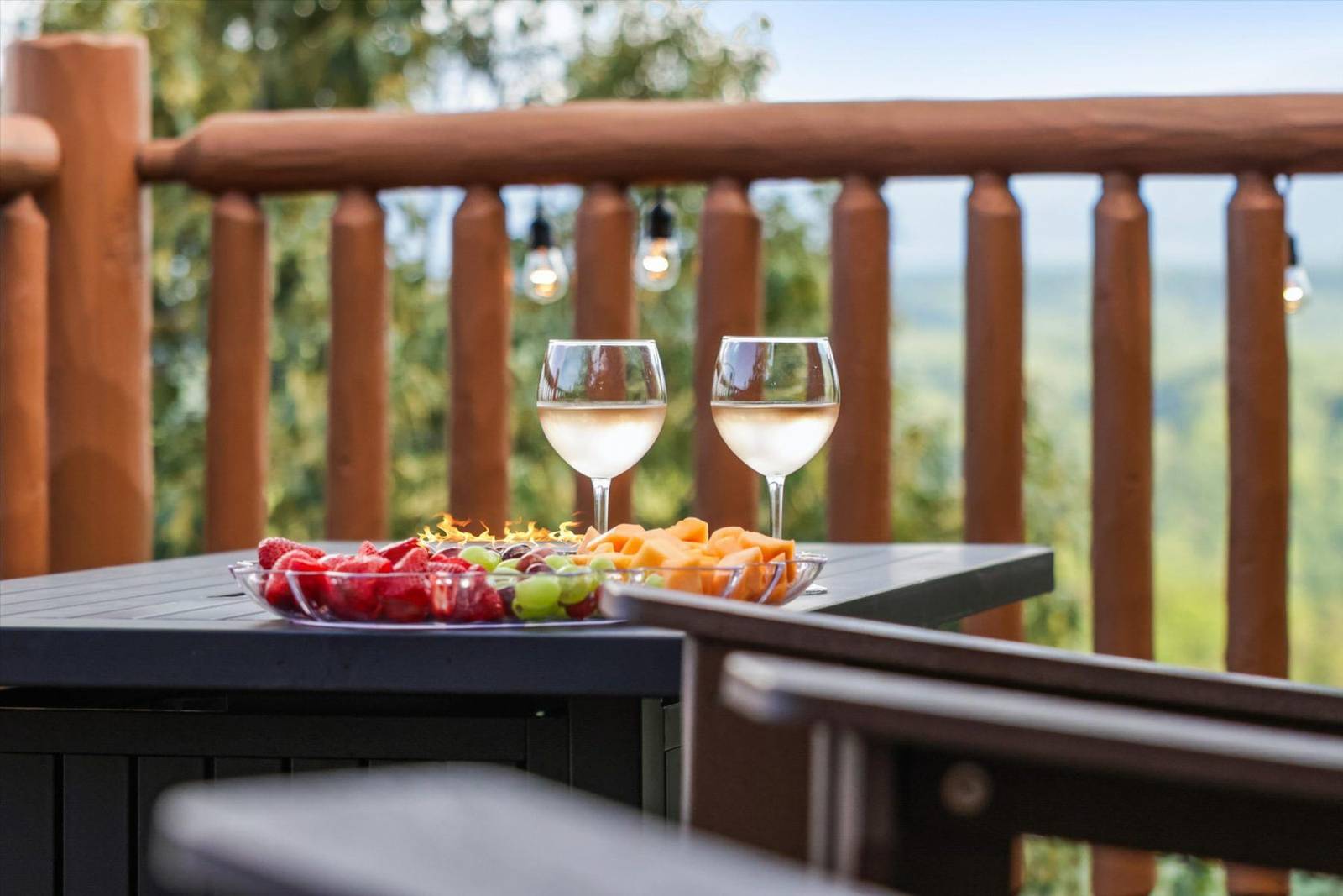 Two wine glasses and fruit plates on a table with a wooden railing