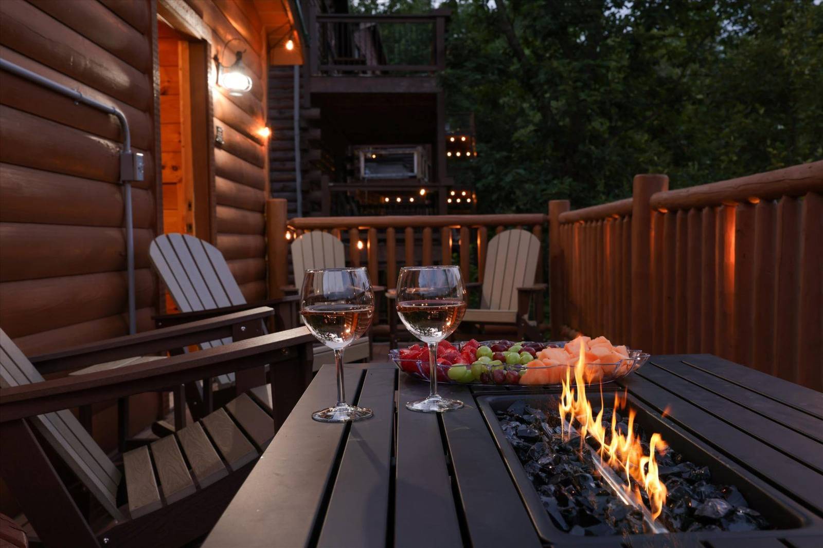 Deck with fire pit, wine glasses, fruit, and Adirondack chairs
