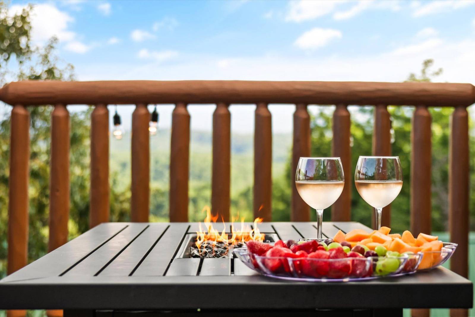 Table with fire pit, wine, fruit, and wooden railing outdoors