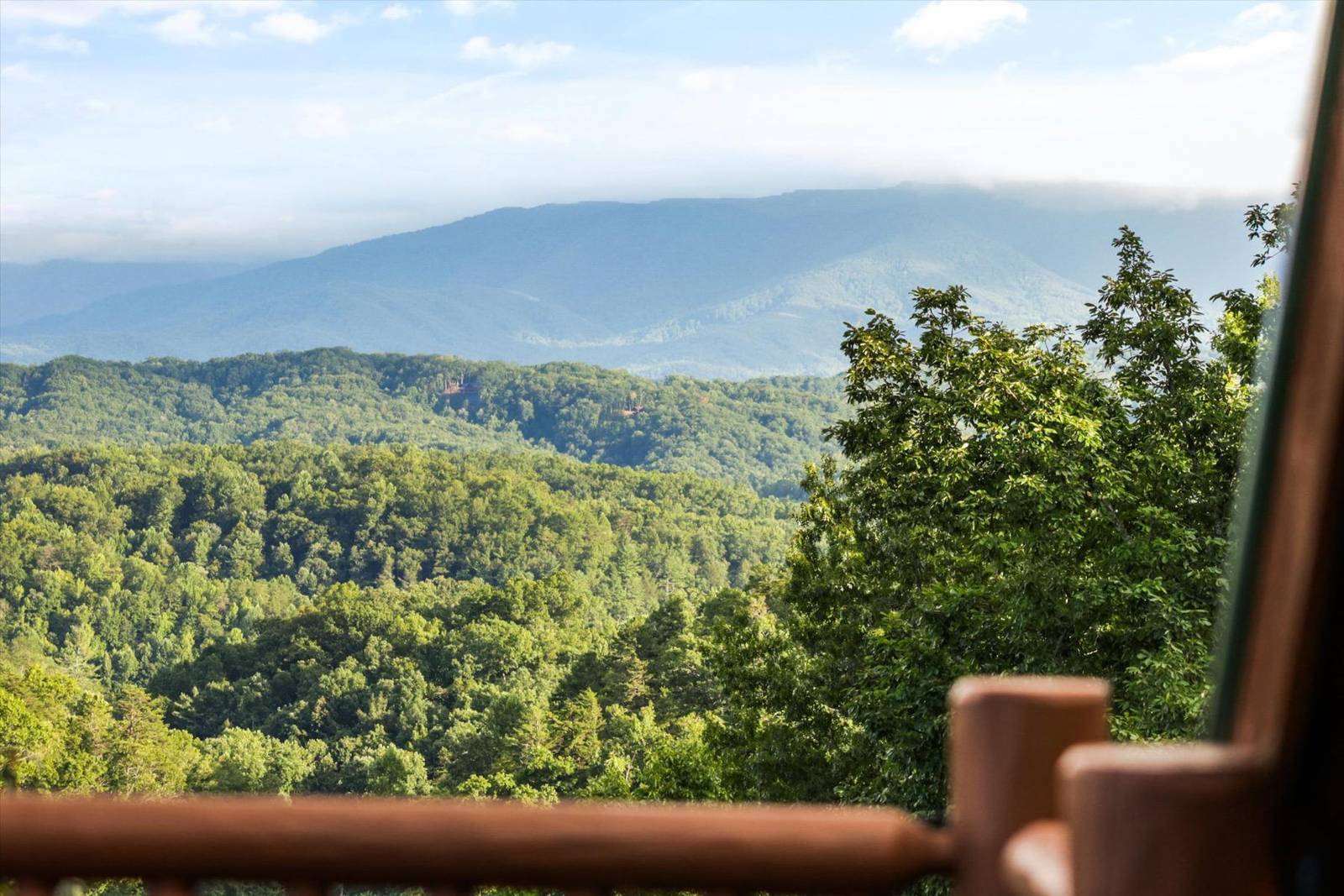 Mountain forest landscape with distant hazy mountains and blue sky, seen from a railing