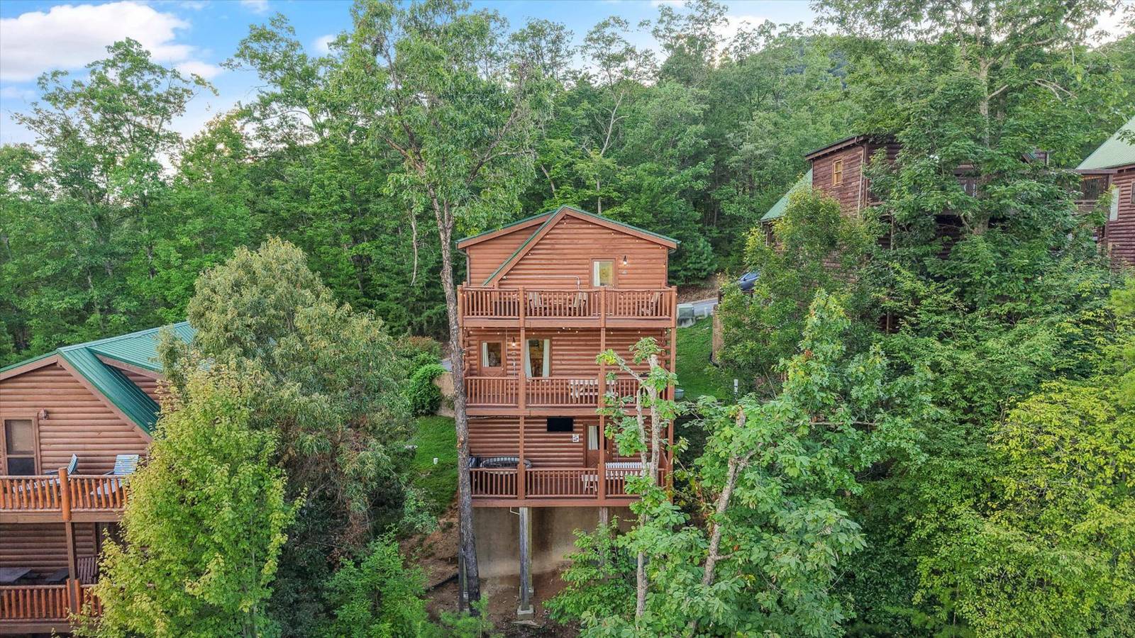 Three-story wooden lodge with multiple decks surrounded by green trees