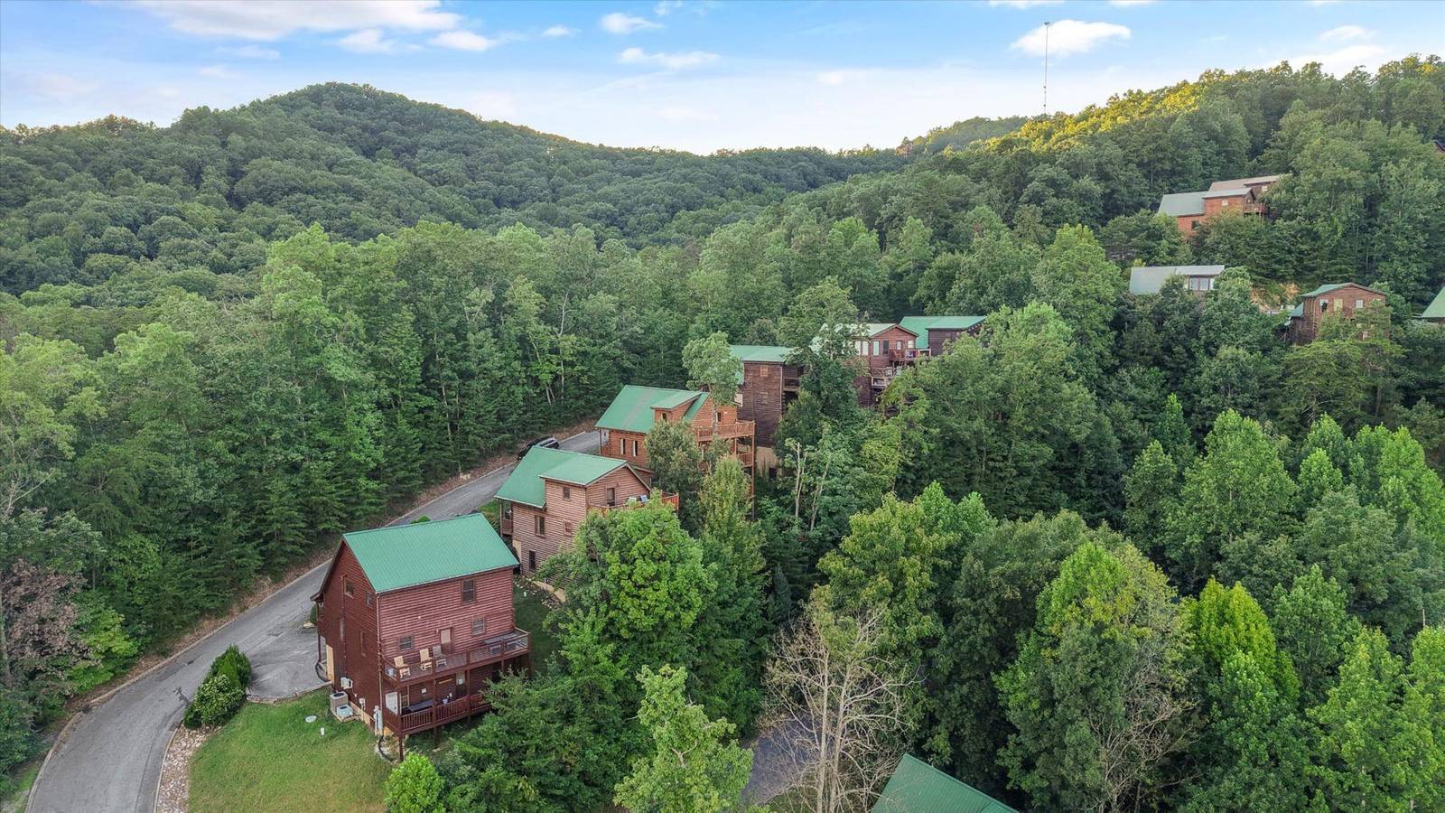 Numerous green-roofed cabins nestled among lush green trees and mountains